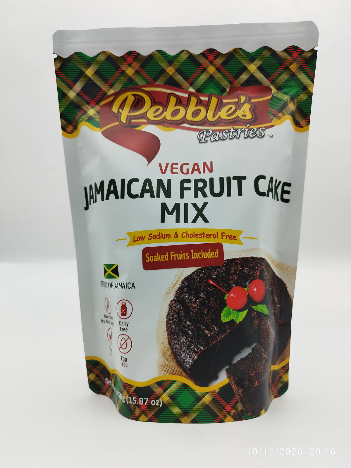 A stand-up pouch of Pebble's Pastries Vegan Jamaican Fruit Cake Mix on a plain white background. The packaging features a white center with black and red text, a picture of a fruit cake with berries, and green and red tartan plaid patterns at the top and bottom.